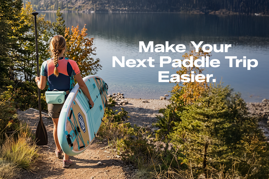 A woman carrying a turquoise paddle board and paddle toward a lake, with the text “Make Your Next Paddle Trip Easier.”
